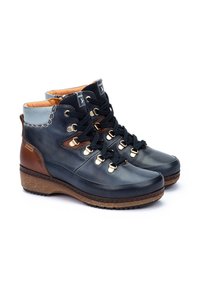 Botas de tobillo de cuero azul con acentos marrones, cordones negros, herrajes dorados y una suela marrón texturizada. Forradas con material naranja.