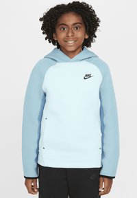 Sudadera azul clara con acentos en azul oscuro, textura suave y un bolsillo frontal. Presenta un logo negro de Nike en la zona izquierda del pecho.