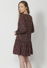 Blumenmuster-Kleid in Schwarz, Rot und Grün; lange Ärmel, runder Halsausschnitt mit einem Schlüsselloch-Rücken und einem mehrlagigen Rüschensaum.