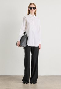 Camicia bianca a bottoni, pantaloni neri a gamba larga, borsa strutturata nera, occhiali da sole neri grandi, texture liscia, design minimalista.