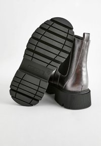 Bottines noires avec un dessus en cuir brillant, des panneaux latéraux élastiques et une semelle en caoutchouc épaisse avec un motif de texture.