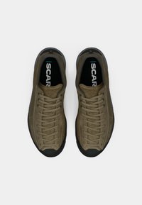 Oliven grønne ruskinds sneakers med sorte gummisåler, der har snørebåndsdesign og logo på indersålen, set ovenfra.