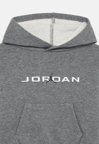 Hoodie gris en tissu doux avec un logo "JORDAN" blanc et une silhouette de jumpman noire. Comprend une poche kangourou à l'avant et une capuche.