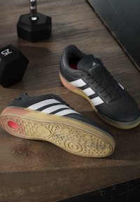 Black athletic shoes with three white stripes, rubber soles featuring circular and textured patterns, and red accents on the inside.