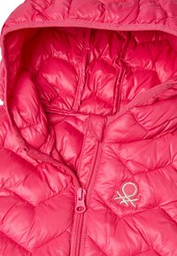 Růžová prošívaná péřovka s kapucí, se zipem vpředu a malým logem na hrudi. Hladký, lesklý povrch.