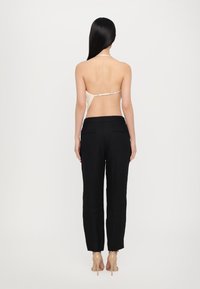 Vedere din spate a unui model care poartă un top halter bej și pantaloni negri, croiți. Outfitul are un design minimalist, cu o textură netedă.