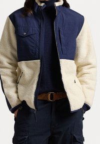 Marineblauwe en crèmekleurige zip-up jack met een textuur fleece lichaam en gladde stof mouwen. Voorzien van drukknopen zakken en een hoge kraag.