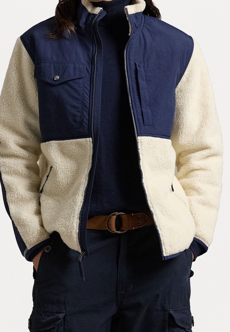 Marineblauwe en crèmekleurige zip-up jack met een textuur fleece lichaam en gladde stof mouwen. Voorzien van drukknopen zakken en een hoge kraag.