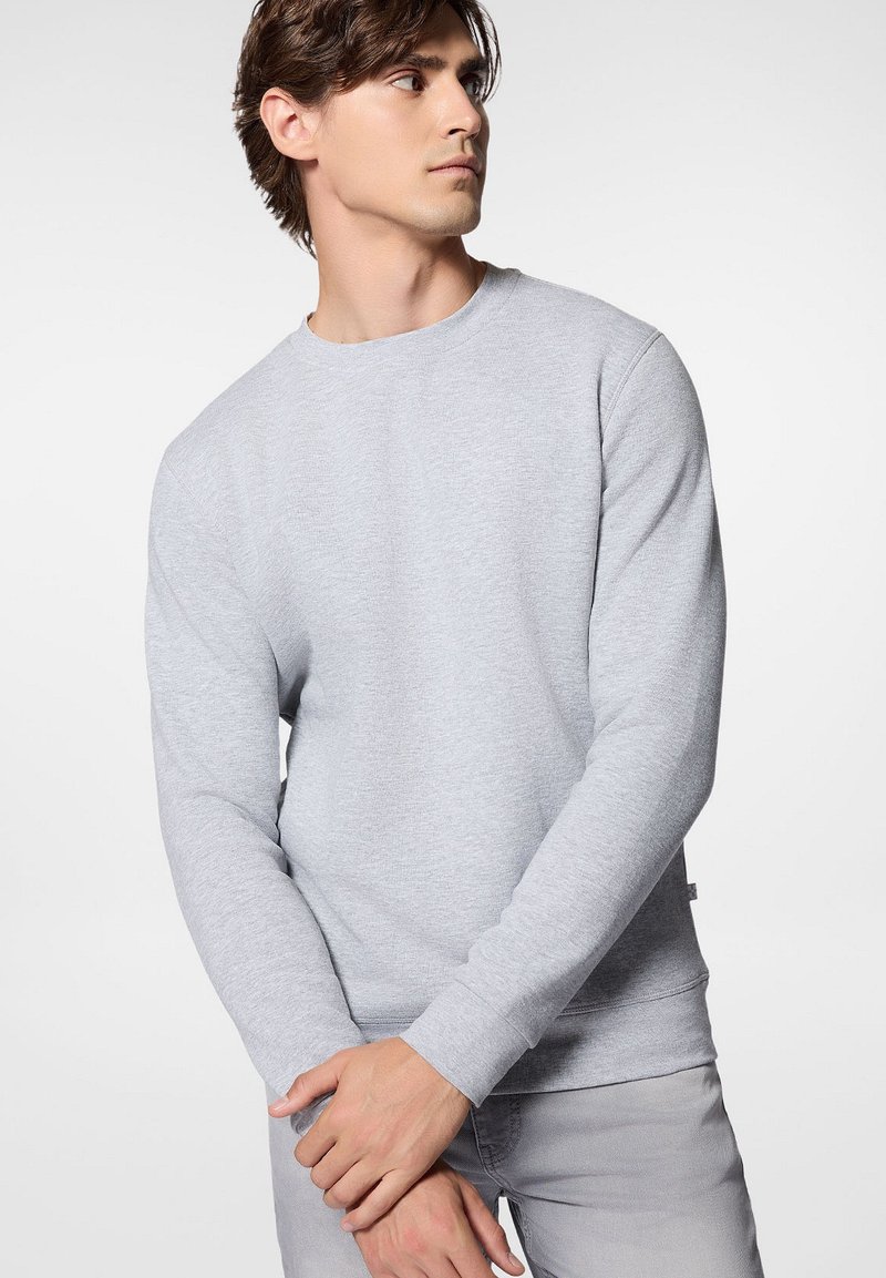 Jasnoszary sweter z miękkiego materiału, wyposażony w okrągły dekolt i długie rękawy, o luźnym kroju i ściągaczach na nadgarstkach.