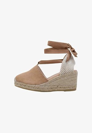 Espadrille à talon en toile marron avec des lanières entrecroisées, détail tissé à l'arrière et base enroulée de jute. Les accents comprennent un nœud à la cheville.