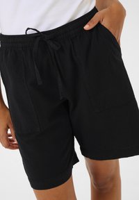 Shorts noirs en tissu léger, dotés d'une taille élastique avec cordon de serrage, de poches latérales et d'une coupe décontractée.