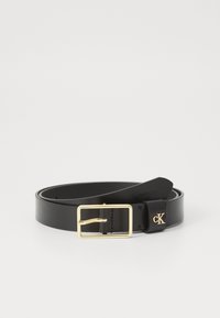 Zwarte leren riem met een glanzende gouden rechthoekige gesp. Beschikt over een gebogen uiteinde en een klein "CK" logo dat op de band is geperst.