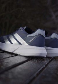 Modré športové topánky s textúrovaným zvrškom, strieborným dizajnom s tromi prúžkami a bielou ľahkou podrážkou označenou "Lightstrike".