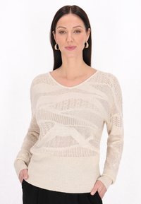 Beżowy sweter dziany z dekoltem w serek, z falistymi wzorami i ściągaczami na rękawach, wykonany z lekkiego materiału dla uzyskania fakturowanego wyglądu.