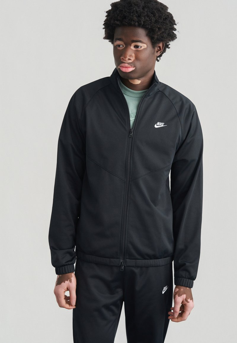 Μαύρο φόρμα της Nike με ζακέτα με φερμουάρ, που διαθ έτει λευκό λογότυπο, ελαστικά μανίκια και αντίστοιχο παντελόνι, κατασκευασμένο από απαλό, ελαφρύ υλικό.