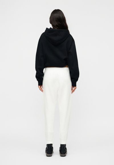 Μαύρο κοντό φούτερ με κουκούλα, σε συνδυασμό με λευκή φόρμα. Το σύνολο έχει χαλαρή εφαρμογή και ριμπ μανσέτες. Μαύρα παπούτσια ολοκληρώνουν την εμφάνιση.