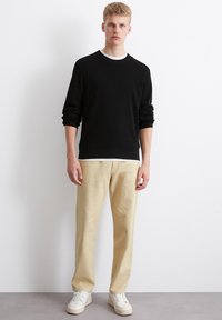 Schwarzer Rippenpullover mit Rundhalsausschnitt, kombiniert mit beigen geraden Hosen und weißen Sneakern. Minimalistisches Design, weicher Stoff.