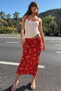 White tank top with red floral pattern and thin straps, paired with a red floral ankle-length skirt. Casual sandals on feet.
