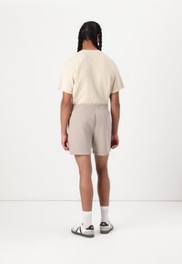 Camiseta de algodón beige y pantalones cortos de algodón gris claro, con una cinturilla elástica. Combinado con calcetines blancos y zapatos con detalles en negro.