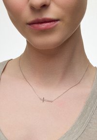 Srebrny wisiorek w kształcie krzyża na cienkim łańcuszku, charakteryzujący się minimalistycznym designem z przecięciem poziomego i pionowego pręta.
