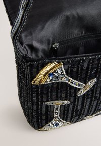 Sac à main noir en perles avec un motif de verre à martini pailleté. Il possède un intérieur en tissu noir lisse et une fermeture éclair.