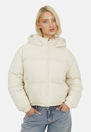 Pufferjack in crème, met een rits aan de voorkant, capuchon met schapenvacht voering, elastische manchetten en een boxy silhouet. Gedirigeerd met lichtblauwe jeans.