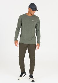 Langsleeve, olijfgroen shirt met een ronde hals en een vaag logo. Gecombineerd met slim-fit, donker olijfkleurige broek en zwarte sportschoenen.