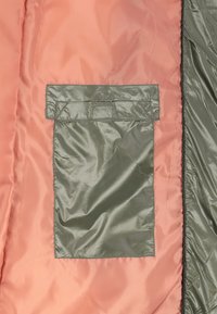 Poche intérieure verte avec rabat sur une doublure en tissu lisse rose et vert.