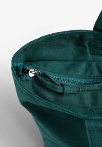 Bolsa de lona verde con cierre de cremallera. Presenta una textura suave y costuras reforzadas a lo largo de los bordes. Interior visible.