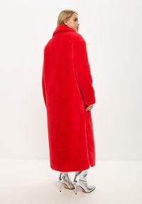 Abrigo largo rojo con una textura suave y aterciopelada y un alto cuello, con mangas largas y un corte holgado, combinado con botas de tobillo plateadas y brillantes.