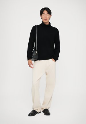 Schwarzer Rollkragenpullover, cremefarbene weit geschnittene Hose, schwarze Lederschuhe und eine kleine schwarze Tasche mit einem Tragegurt. Schlichtes und modernes Design.