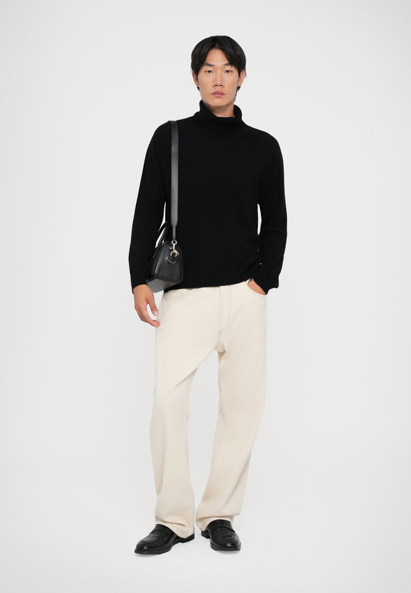 Maglione a collo alto nero, pantaloni beige a gamba larga, scarpe di pelle nere e una piccola borsa nera con tracolla. Design semplice e moderno.