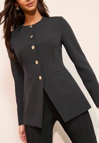 Czarna dopasowana marynarka z wysokim kołnierzem, złotymi guzikami w kształcie kwiatów, o wąskim kroju i bocznymi kieszeniami; gładka tekstura i strukturalny design.