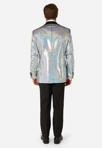 Lesklá strieborná blazerka s flitrami a zadným rozparkom, kombinovaná s čiernymi nohavicami a topánkami. Flitre odrážajú rôzne farby pri svetle.