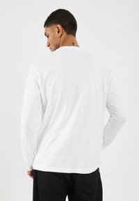 Λευκό T-shirt με μακριά μανίκια, φτιαγμένο από βαμβάκι, με στρογγυλή λαιμόκοψη και άνετη εφαρμογή, ορατές ραφές και λεία υφή.