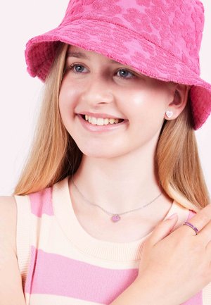 Chapeau de seau rose avec un motif texturé, haut rayé rose et crème, collier et boucles d'oreilles en forme de cœur, et une bague violette.