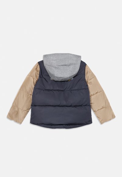 Vadderad jacka med grå huva, marinblå rygg och beigefärgade ärmar. Slät yta med synlig sömnad och en logopatch på ryggen.