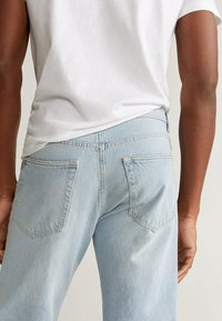 Unos vaqueros de denim azul claro presentan un corte recto, dos bolsillos traseros y costuras básicas, combinados con una camiseta blanca sencilla.