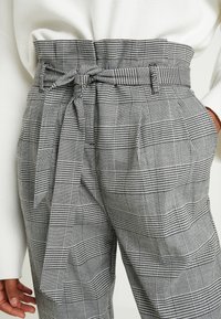 Gray plaid trousers with a high waist, feature a fabric belt and pockets; a mix of check patterns in black and white tones.