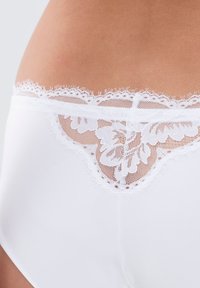 Witte panties met een bloemige kantafwerking aan de tailleband, een gladde stoffen body en delicate gegolfde randen.