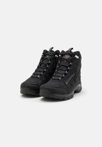 Black insulated hiking boots with quilted fabric, rugged sole, and lace-up design featuring reflective accents and branded logo on the side.