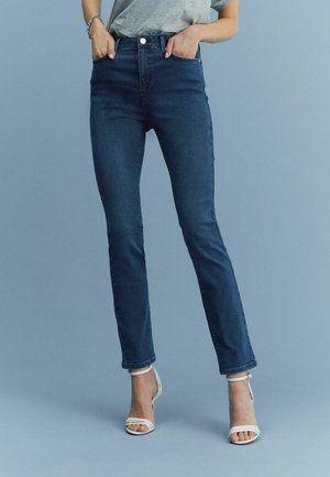 Siniset korkeavyötäröiset farkut slim fit -mallilla, joissa on etupainike, viisi taskua ja huomaamatonta tikkiväriä. Yhdistettynä valkoisiin sandaaleihin.