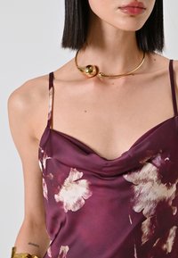 Camisole in satin di un profondo bordeaux con un motivo floreale in crema e rosa chiaro; abbinato a un collier in metallo dorato.