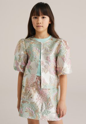 Niña con cabello lacio que lleva una chaqueta brocada con flores a juego, con mangas abullonadas, y falda en tonos pastel verde, rosa y dorado.