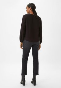 Black long-sleeve top with a rounded hem, paired with dark denim pants. The outfit features a simple, clean design and fitted silhouette.