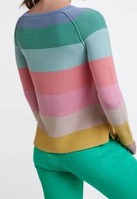 Maglione a righe multicolore in blu, verde, rosa e giallo, con una texture a coste e una scollatura rotonda; abbinato a pantaloni verdi.