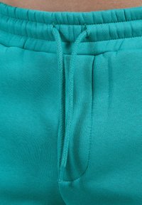 Pantalones de chándal turquesa con cordón, con cintura elástica, que cuentan con bolsillos laterales y una textura de tela suave.