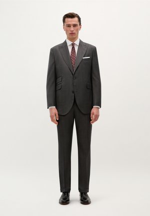 Traje gris a rayas con solapas muesca, dos botones, camisa de vestir blanca y corbata roja con patrón, combinado con zapatos de cuero negros.