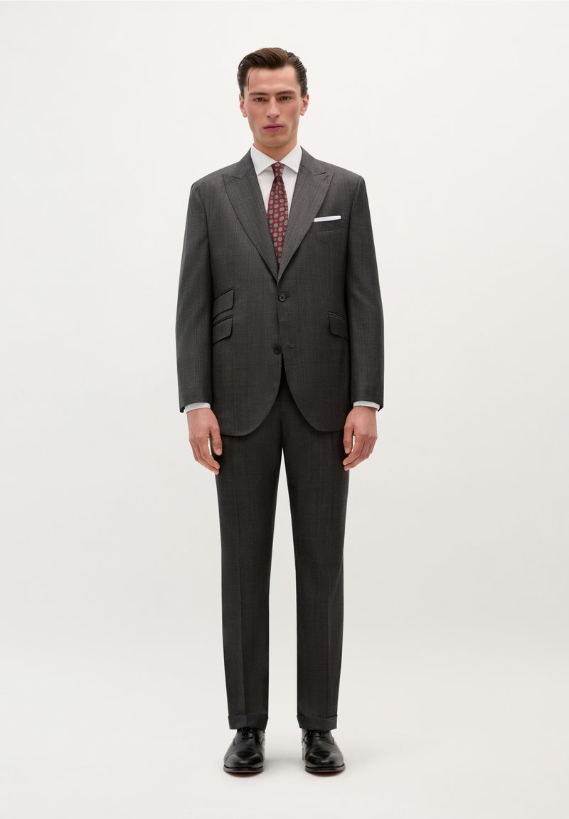 Traje gris a rayas con solapas muesca, dos botones, camisa de vestir blanca y corbata roja con patrón, combinado con zapatos de cuero negros.
