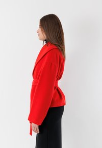 Giacca avvolgente rossa in lana con ampi rever, vita cintrata e maniche lunghe. Design a tinta unita, texture morbida, taglio aderente in vita.